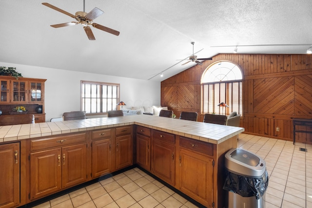 kitchen featuring vaulted ceiling, tile countertops, wooden walls, light tile patterned floors, and kitchen peninsula