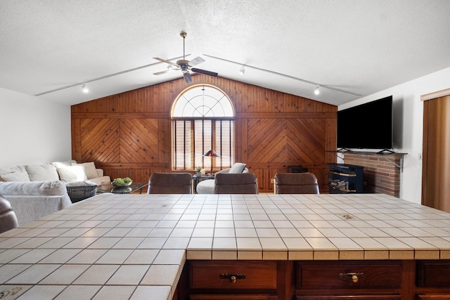 interior space with tile counters, wooden walls, ceiling fan, and vaulted ceiling