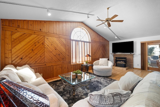 living room with wooden walls, a fireplace, a textured ceiling, light tile patterned flooring, and vaulted ceiling