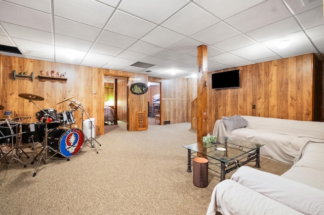 living room featuring carpet flooring, a drop ceiling, and wooden walls