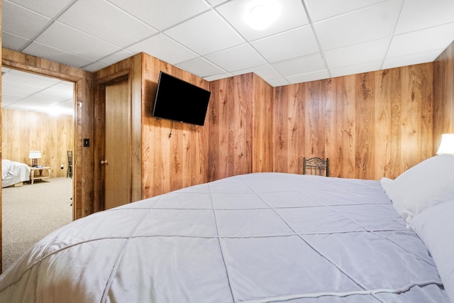 bedroom with a drop ceiling, carpet, and wood walls