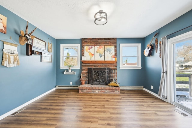 unfurnished living room with hardwood / wood-style flooring, a baseboard radiator, a brick fireplace, and a wealth of natural light