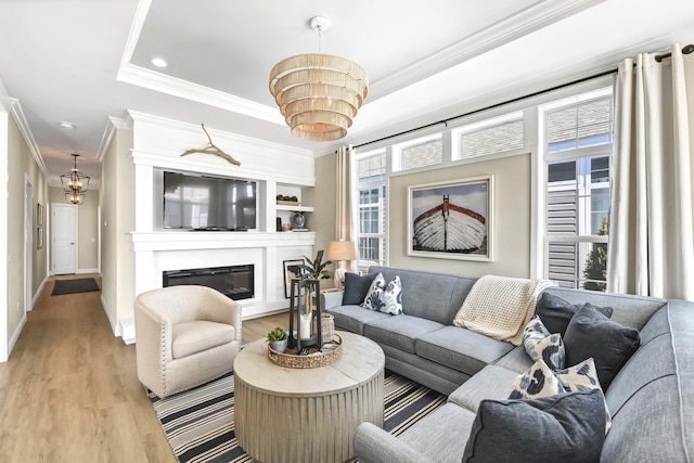 living room featuring a tray ceiling, ornamental molding, a chandelier, and light wood-type flooring