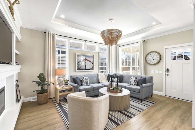 living room with a raised ceiling, ornamental molding, and light hardwood / wood-style floors