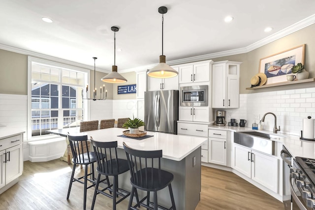 kitchen featuring sink, white cabinetry, appliances with stainless steel finishes, a kitchen island, and pendant lighting