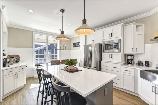 kitchen featuring white cabinetry, a kitchen breakfast bar, a kitchen island, pendant lighting, and stainless steel appliances