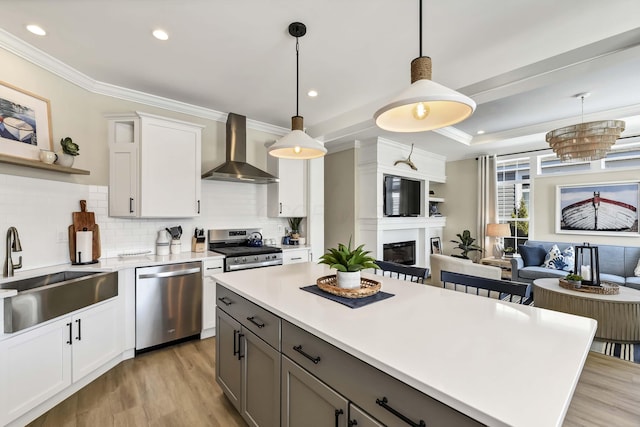 kitchen with sink, white cabinetry, decorative light fixtures, stainless steel appliances, and wall chimney range hood