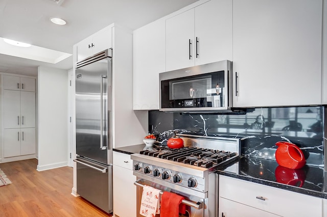 kitchen featuring white cabinetry, dark stone countertops, backsplash, light hardwood / wood-style floors, and stainless steel appliances