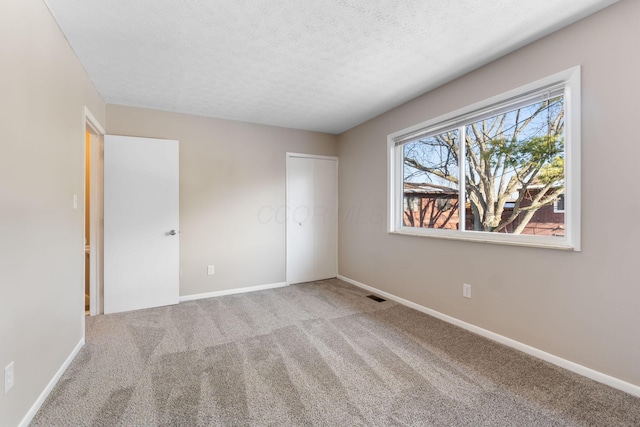 unfurnished bedroom featuring light carpet, a textured ceiling, and a closet