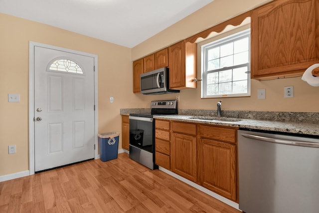 kitchen featuring stone countertops, appliances with stainless steel finishes, sink, and light wood-type flooring