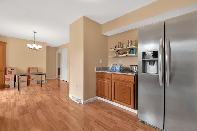 kitchen featuring hanging light fixtures, stainless steel refrigerator with ice dispenser, light stone countertops, a chandelier, and light wood-type flooring