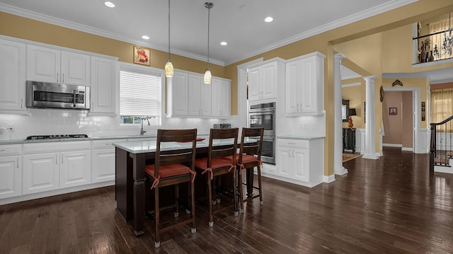 kitchen with appliances with stainless steel finishes, hanging light fixtures, white cabinets, a kitchen island, and ornate columns