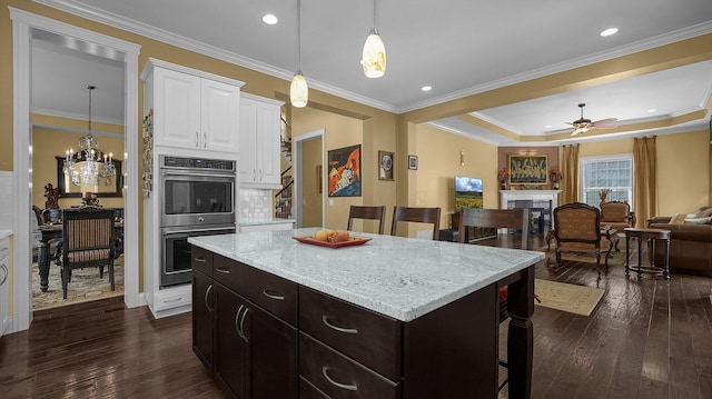 kitchen with dark wood-type flooring, a kitchen bar, white cabinetry, double oven, and a kitchen island