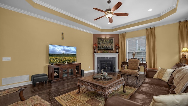 living room featuring a tray ceiling, ornamental molding, dark hardwood / wood-style floors, and ceiling fan