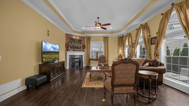 living room with a tray ceiling, dark wood-type flooring, ornamental molding, and ceiling fan