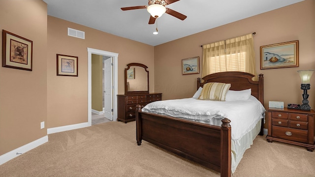 bedroom with ceiling fan, light colored carpet, and ensuite bath