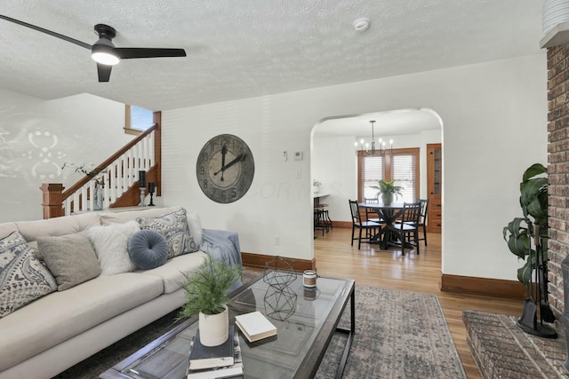 living room featuring ceiling fan with notable chandelier, wood-type flooring, and a textured ceiling