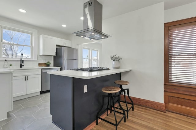 kitchen with a breakfast bar area, white cabinets, island exhaust hood, kitchen peninsula, and stainless steel appliances