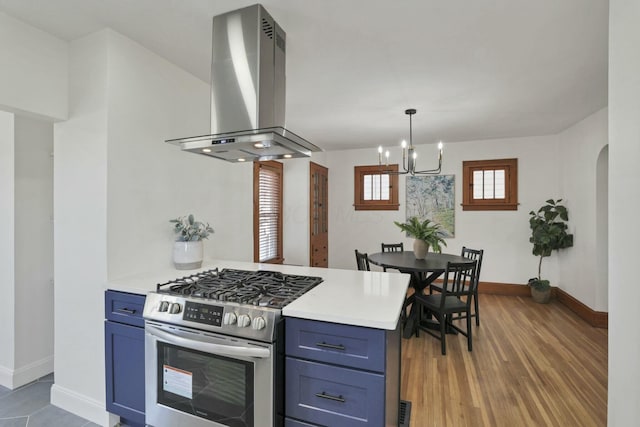 kitchen featuring blue cabinets, island range hood, decorative light fixtures, stainless steel range with gas cooktop, and kitchen peninsula