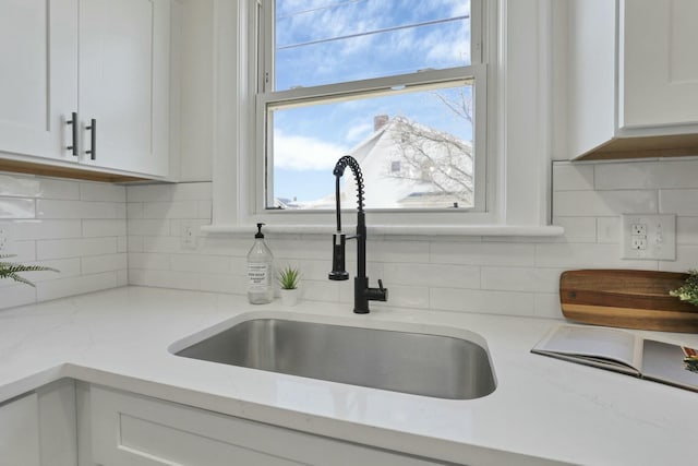 room details with white cabinetry, light stone counters, sink, and tasteful backsplash