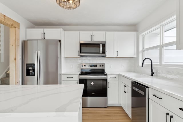 kitchen with stainless steel appliances, white cabinetry, sink, and light stone counters