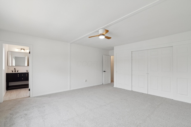 unfurnished bedroom featuring a closet, ensuite bathroom, ceiling fan, and carpet