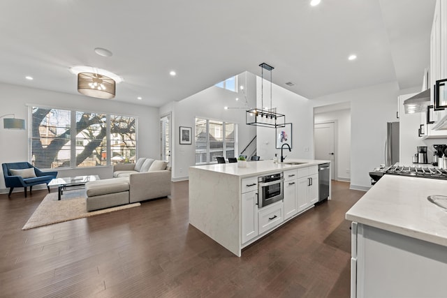 kitchen with sink, white cabinetry, stainless steel appliances, light stone countertops, and a kitchen island with sink