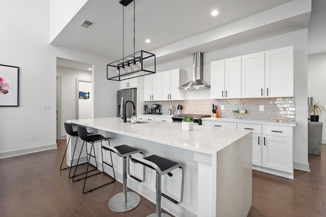 kitchen with white cabinets, stove, an island with sink, and wall chimney range hood