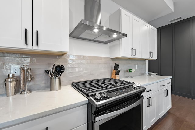 kitchen featuring wall chimney exhaust hood, stainless steel gas range oven, light stone counters, backsplash, and white cabinets