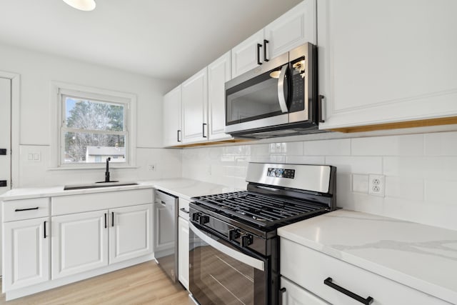 kitchen with sink, white cabinets, decorative backsplash, light hardwood / wood-style floors, and stainless steel appliances