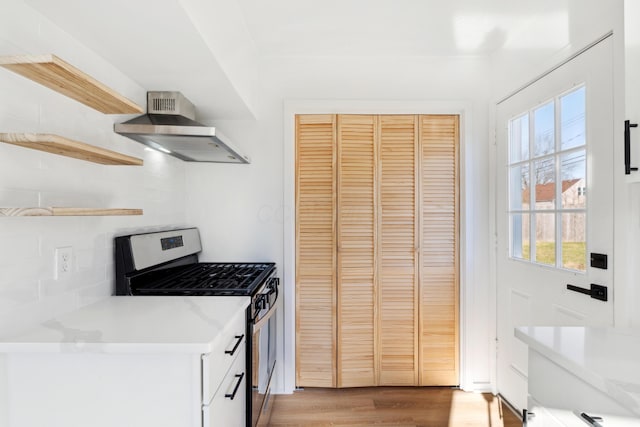 kitchen with white cabinets, wall chimney exhaust hood, light stone counters, stainless steel gas range, and light hardwood / wood-style flooring