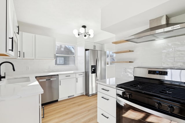 kitchen with sink, white cabinetry, light hardwood / wood-style flooring, stainless steel appliances, and wall chimney range hood