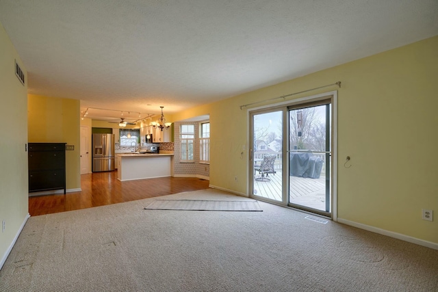 unfurnished living room featuring light colored carpet, a textured ceiling, and a chandelier