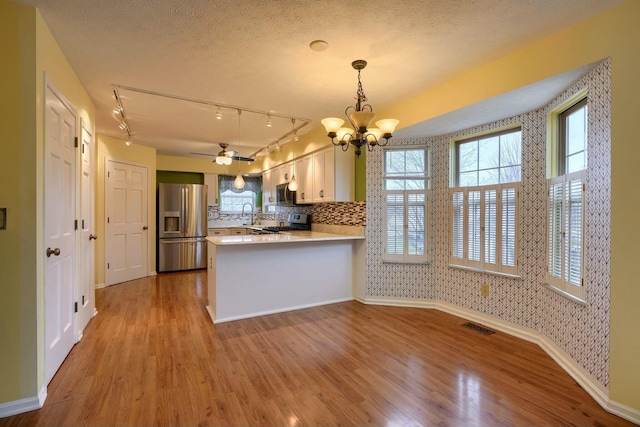 kitchen featuring stainless steel appliances, a textured ceiling, decorative light fixtures, kitchen peninsula, and light wood-type flooring