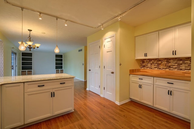 kitchen featuring light wood-type flooring, backsplash, white cabinets, hanging light fixtures, and an inviting chandelier