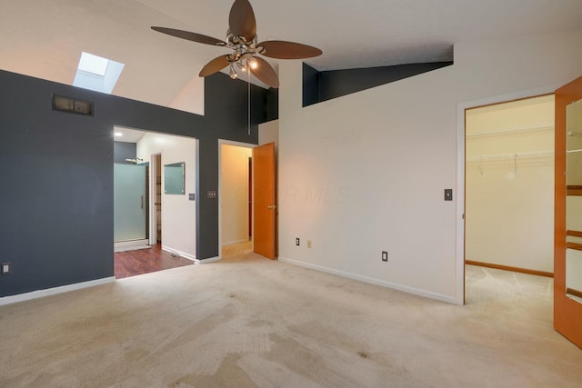 carpeted empty room featuring ceiling fan, high vaulted ceiling, and a skylight