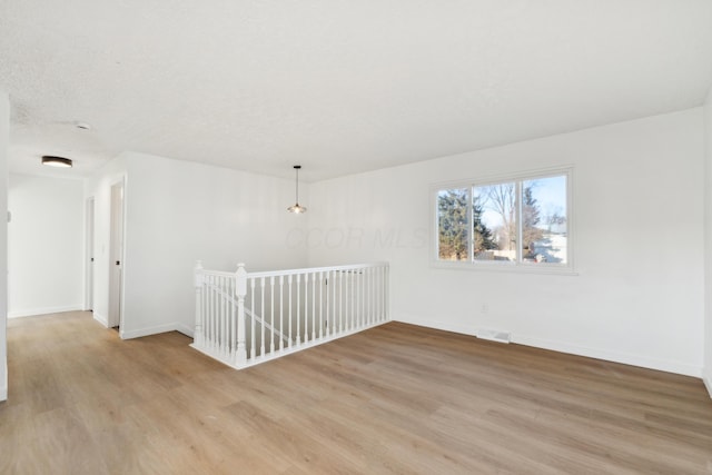 unfurnished room with a textured ceiling and light wood-type flooring