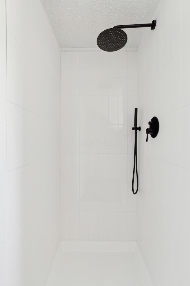 interior details featuring a textured ceiling and tiled shower