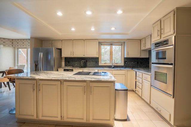 kitchen featuring a kitchen island, appliances with stainless steel finishes, cream cabinets, sink, and light stone countertops