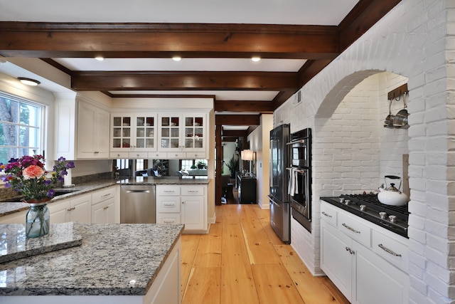 kitchen with white cabinetry, dark stone countertops, beamed ceiling, stainless steel appliances, and light hardwood / wood-style floors