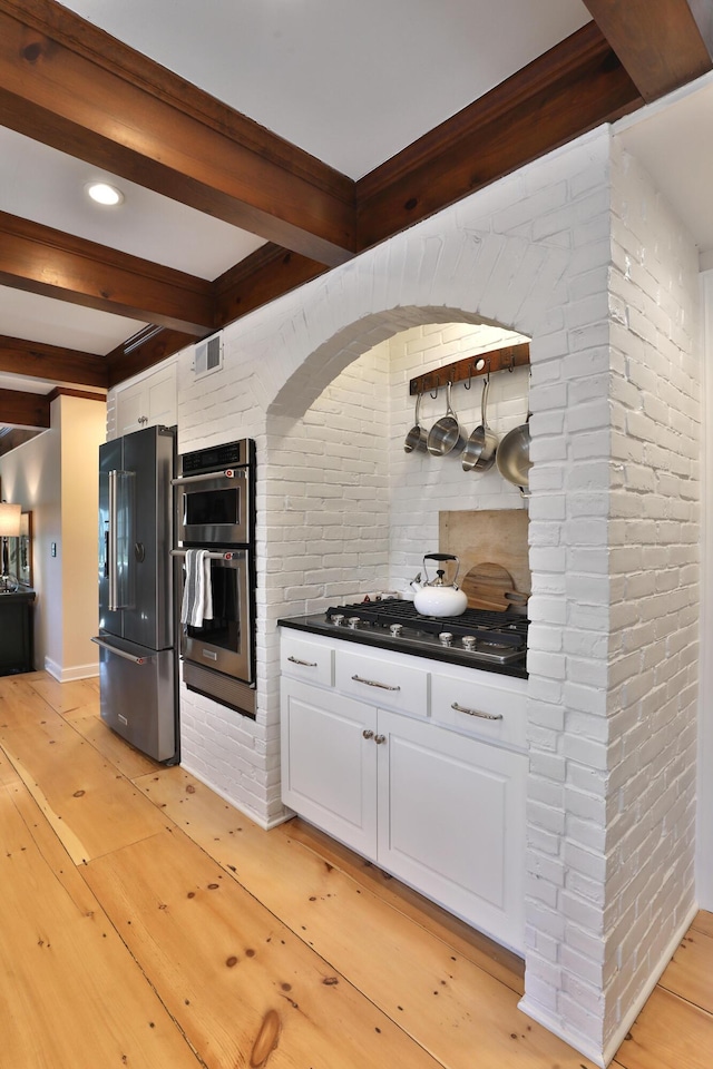 kitchen with stainless steel appliances, white cabinetry, beam ceiling, and light hardwood / wood-style flooring