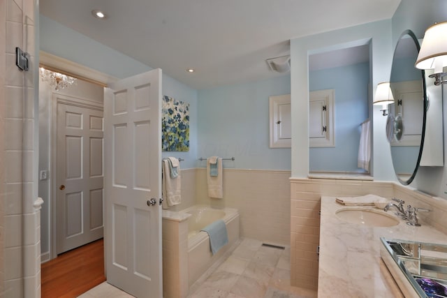 bathroom featuring vanity, a bath, and tile walls