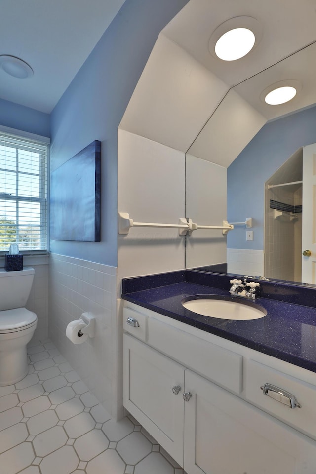 bathroom with lofted ceiling, tile walls, vanity, toilet, and walk in shower