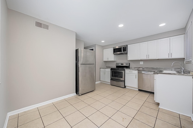 kitchen with appliances with stainless steel finishes, sink, light tile patterned floors, and white cabinets