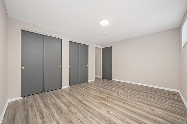 unfurnished bedroom featuring light wood-type flooring and two closets