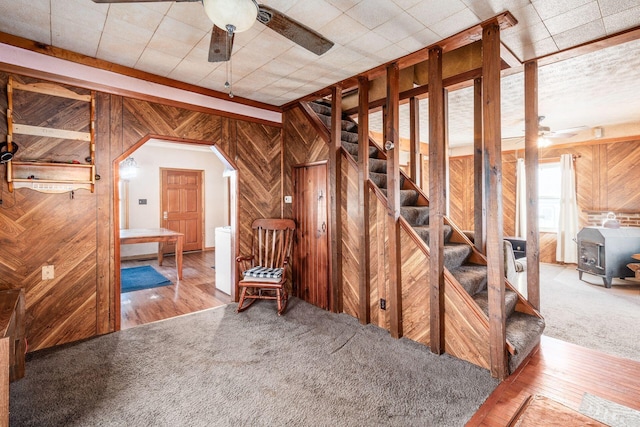 interior space featuring wooden walls, a wood stove, ceiling fan, and carpet