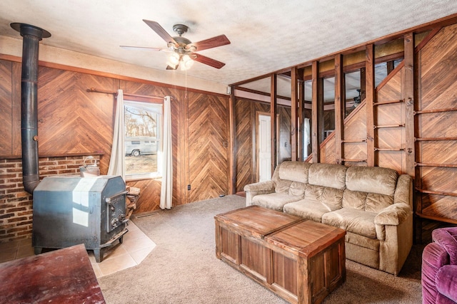 living room featuring wood walls, light colored carpet, a textured ceiling, a wood stove, and ceiling fan