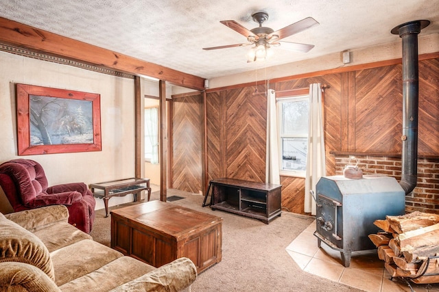 carpeted living room with ceiling fan, a wood stove, wooden walls, and a textured ceiling