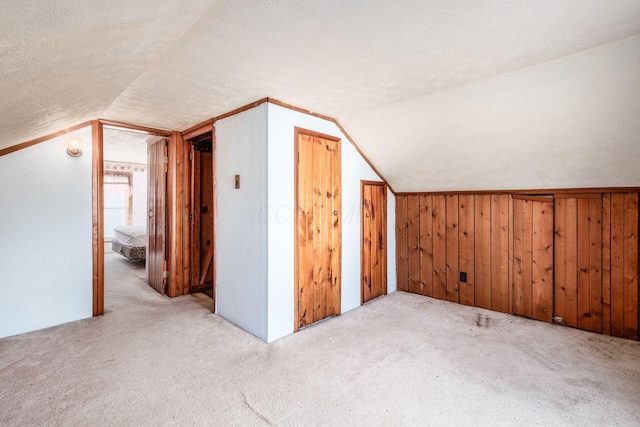 additional living space with vaulted ceiling, wooden walls, light carpet, and a textured ceiling