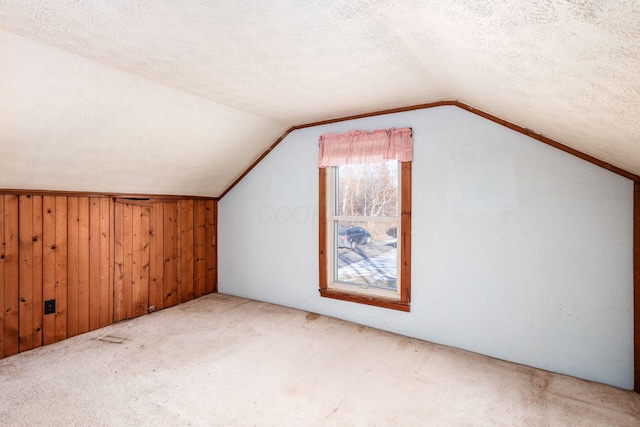 bonus room featuring lofted ceiling, carpet flooring, a textured ceiling, and wood walls